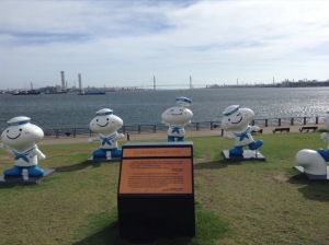 Small smiling statues of sailors, in a semi-circle, by the waterside