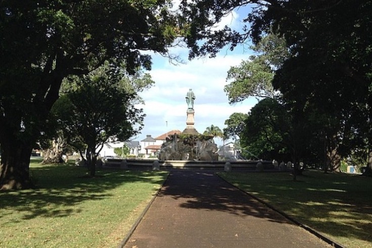 A path leads to a statue on a tall plinth at the entrance to the park