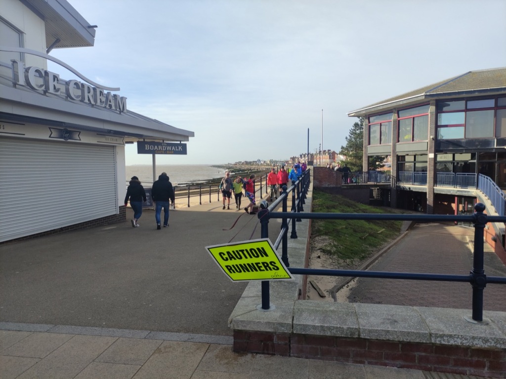 Picture of the Felixstowe promenade, with a caution runners sign on the railings and an ice cream stall on the other side.