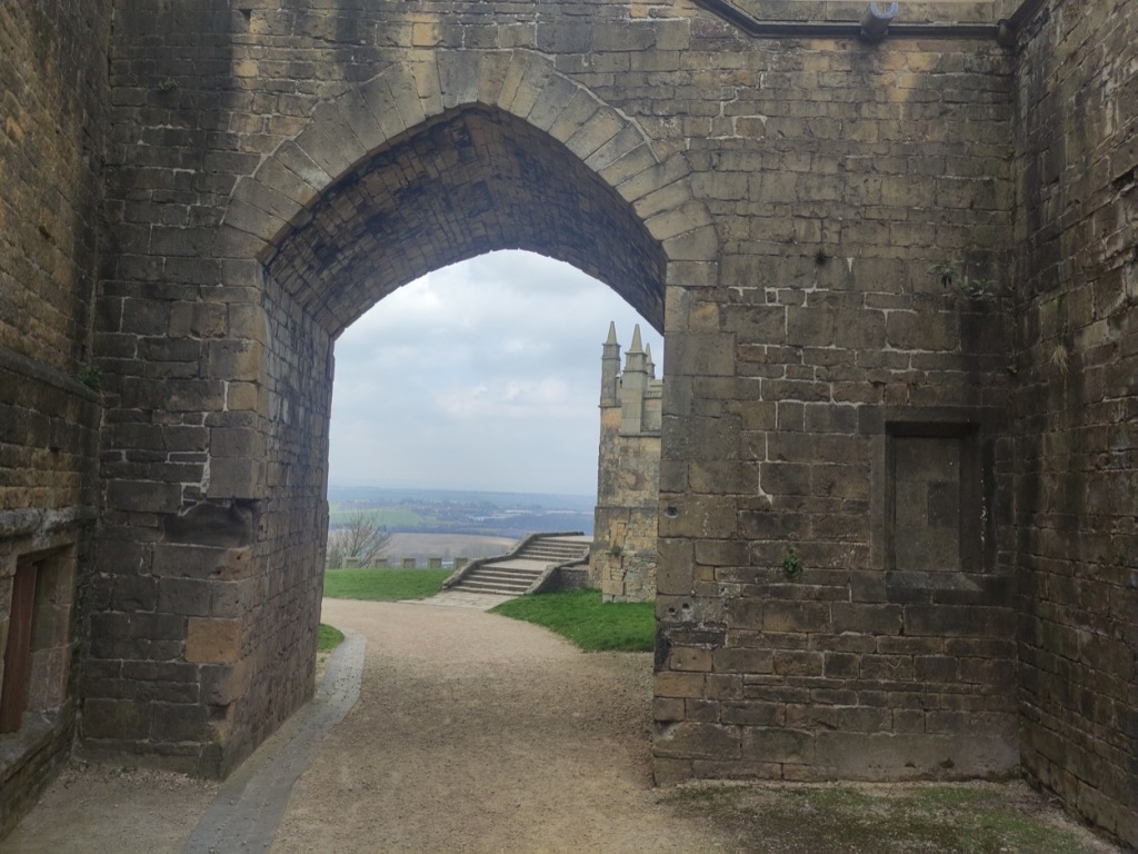 Looking through a 'v' shaped archway  to a wall, stairs and then countryside behind