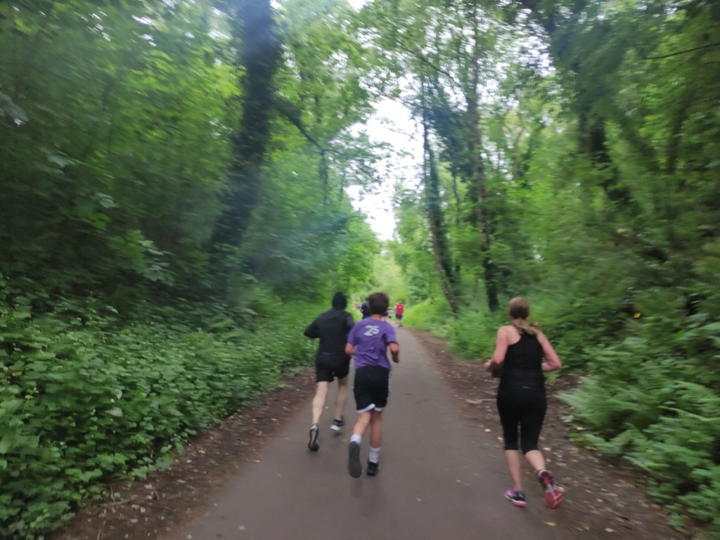 Slightly blurred photo of runners in motion, the path is surrounded by trees, with the blurring making it appear even more green than it is really (which its very green).