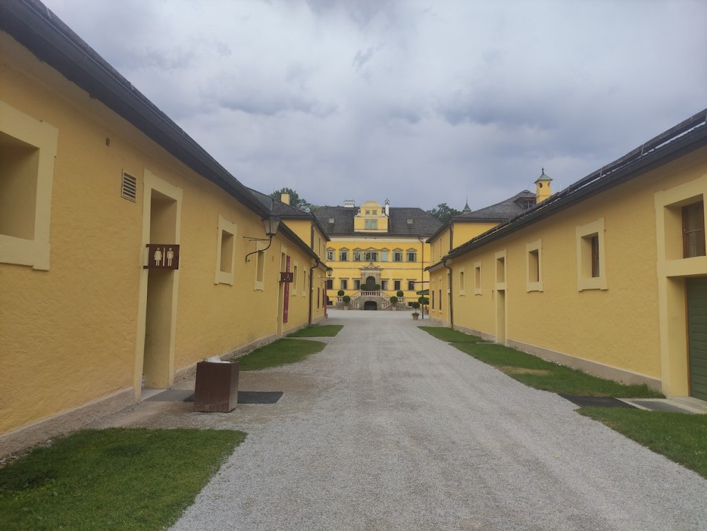 Sandy-yellow painted buildings on either side of the path leading to the palace, a three-storey building with short staircase for entry.