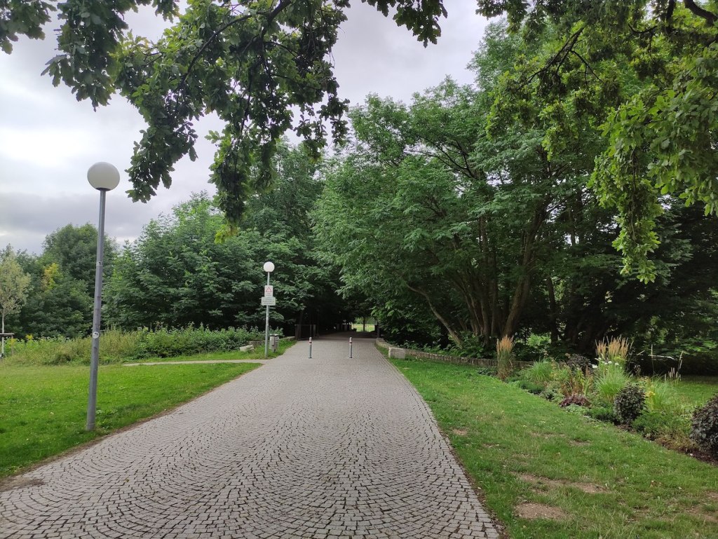 A wide cobbled path heads into a tree-covered area which hides a bridge over the park's lakes.