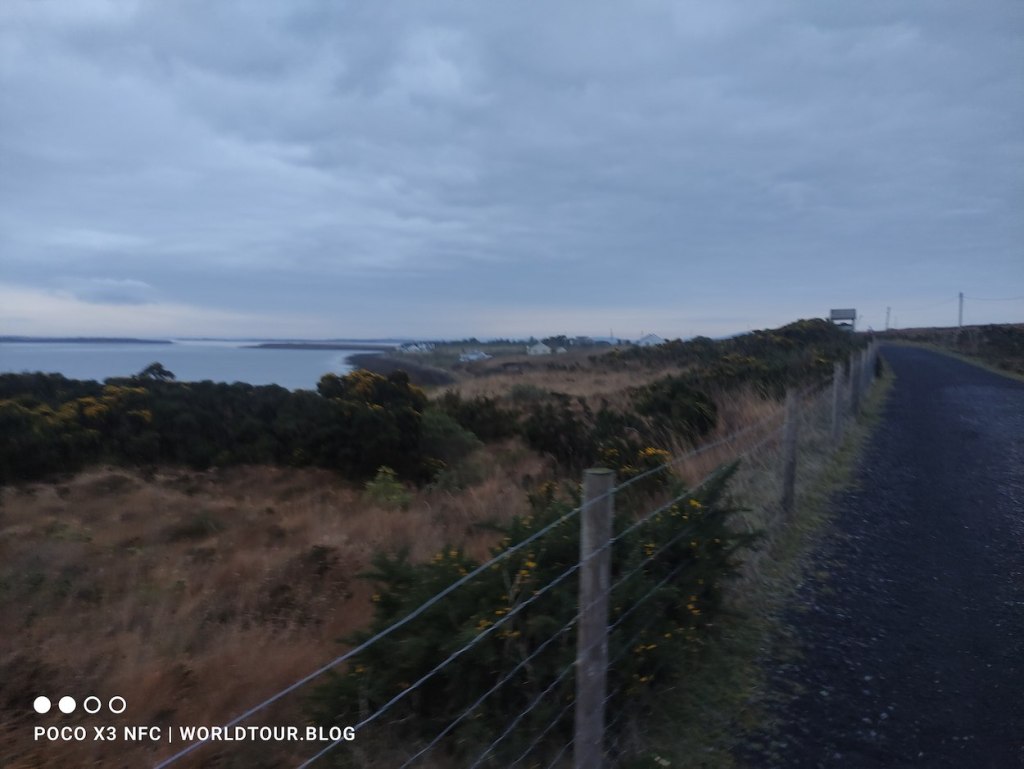 A barbed-wire fence marks the edge of the path, with views over greenery to the sea.